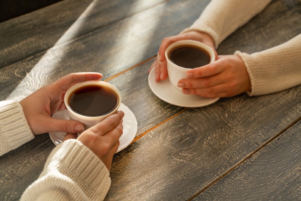 Female hands holding cups of coffee on wooden table background